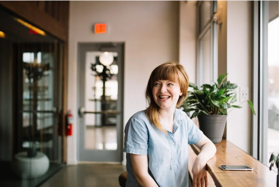woman sitting at a table near a window, smiling