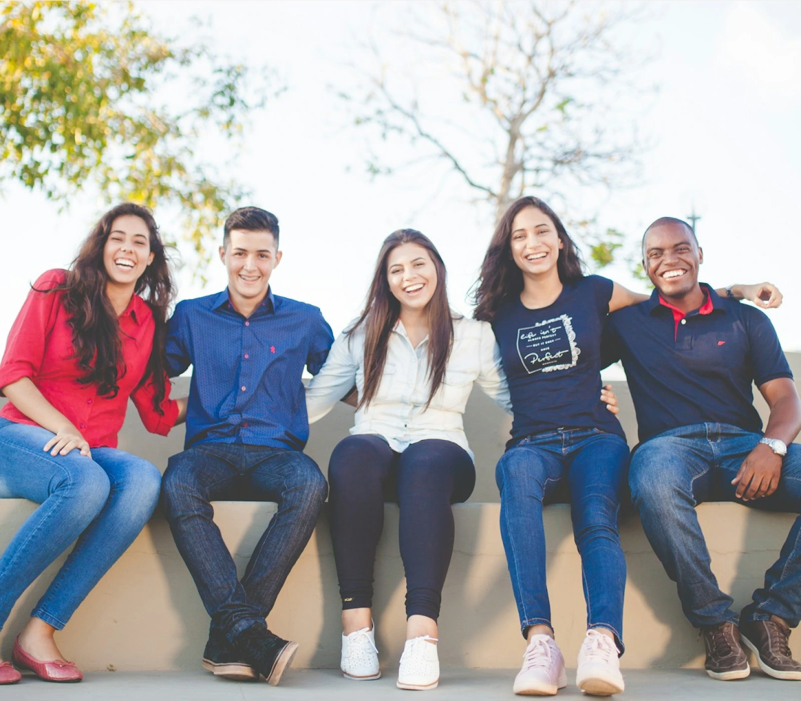 Group of people sitting on a bench outside smiling