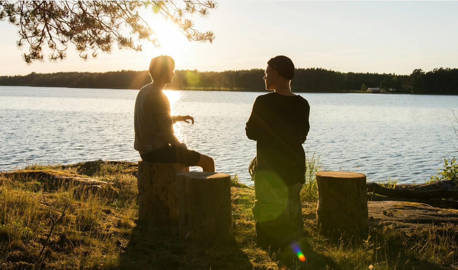2 people sitting near a river over sunset